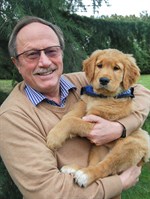 Bill Thornton sitting and holding a golden retriever puppy.