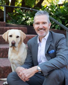 Man in a grey suit sitting next to a golden labrador