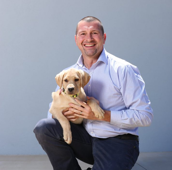 Man kneeling with a golden labrador puppy on knee